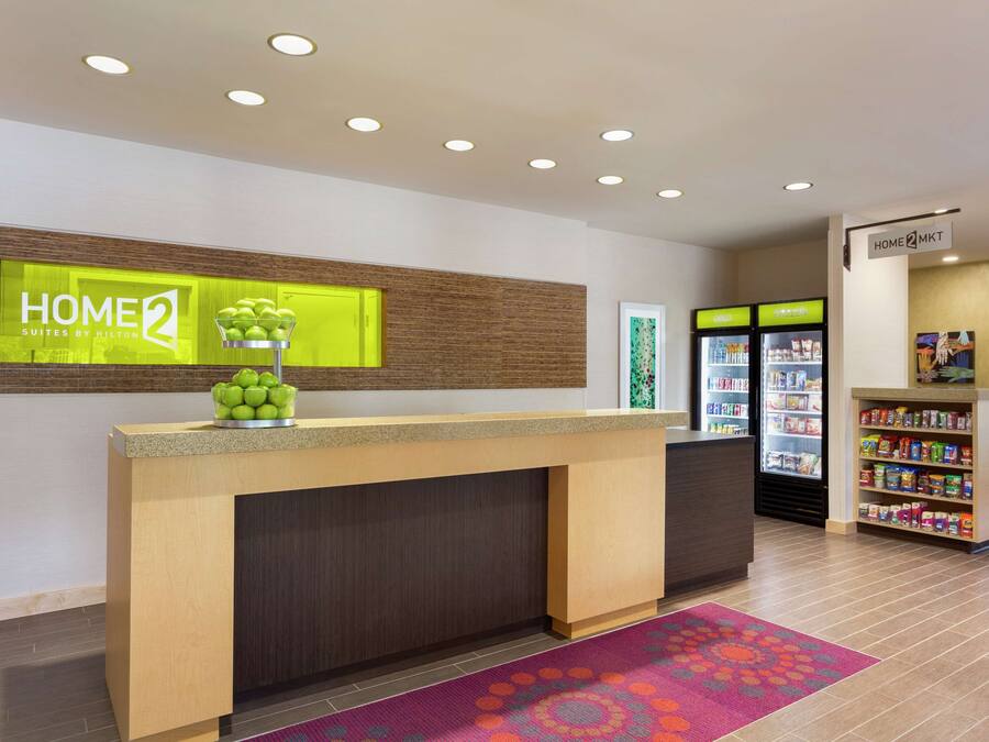 A hotel reception area with a reception desk, a fruit bowl, a refrigerator, and a snack bar.