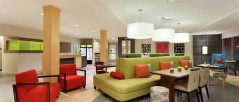 A modern indoor seating area with a green sofa, red chairs, and a dining table with chairs.