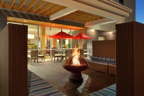 An outdoor seating area with wicker furniture, a fire feature, and red umbrellas. - Home2 Suites by Hilton Lehi/Thanksgiving Point (Lehi)