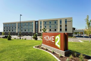 A modern hotel building with a sign reading "HOME 2 Suites by Hilton".