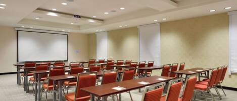 A conference room with rows of tables and chairs, a projector screen, and a whiteboard.