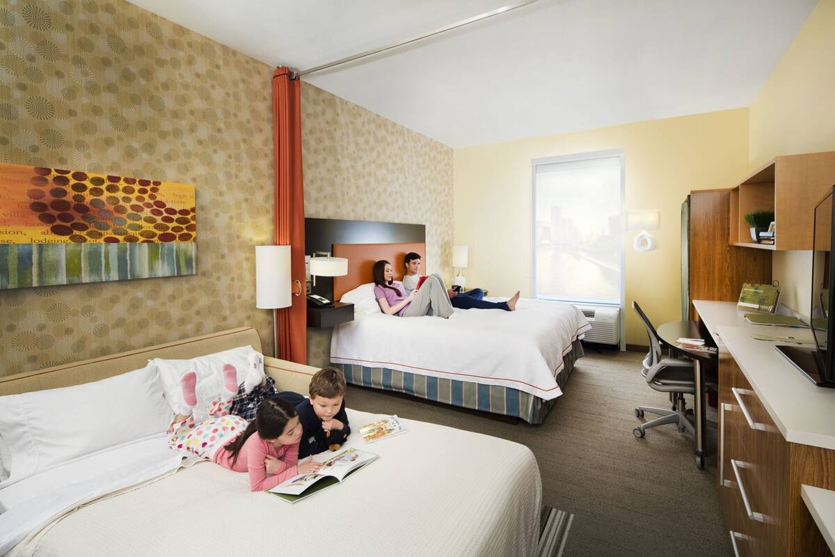 A hotel room with two beds, a desk, a chair, a TV, and a window.