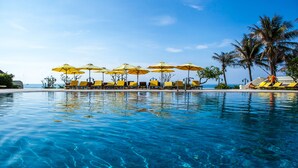 En klarblå pool med solstolar och parasoller, palmer och utsikt över havet.