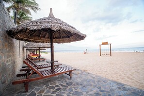 A beachside area with thatched umbrellas, wooden lounge chairs, and a stone-paved walkway. - Allezboo Beach Resort & Spa (Mui Ne)