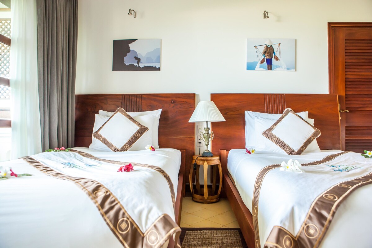 A hotel room with two beds, a nightstand with a lamp, and artwork on the walls.