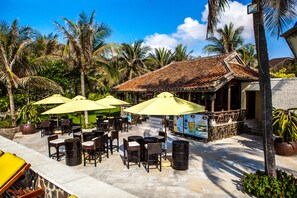 An outdoor patio area with tables and chairs, yellow umbrellas, and a building with a tiled roof. - Allezboo Beach Resort & Spa (Mui Ne)
