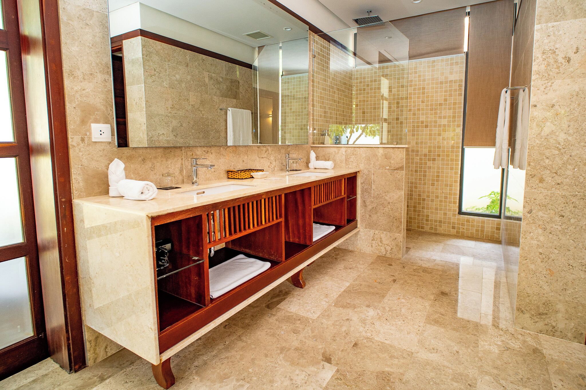 Een moderne badkamer met een grote spiegel, twee wasbakken, een badkamermeubel met planken en een douchegedeelte.