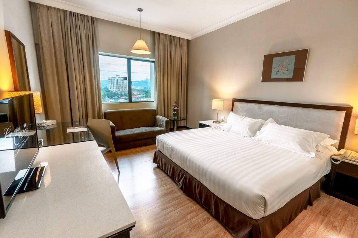 Une chambre d’hôtel avec un grand lit, un bureau, une chaise, une lampe et une vue sur la ville par la fenêtre.