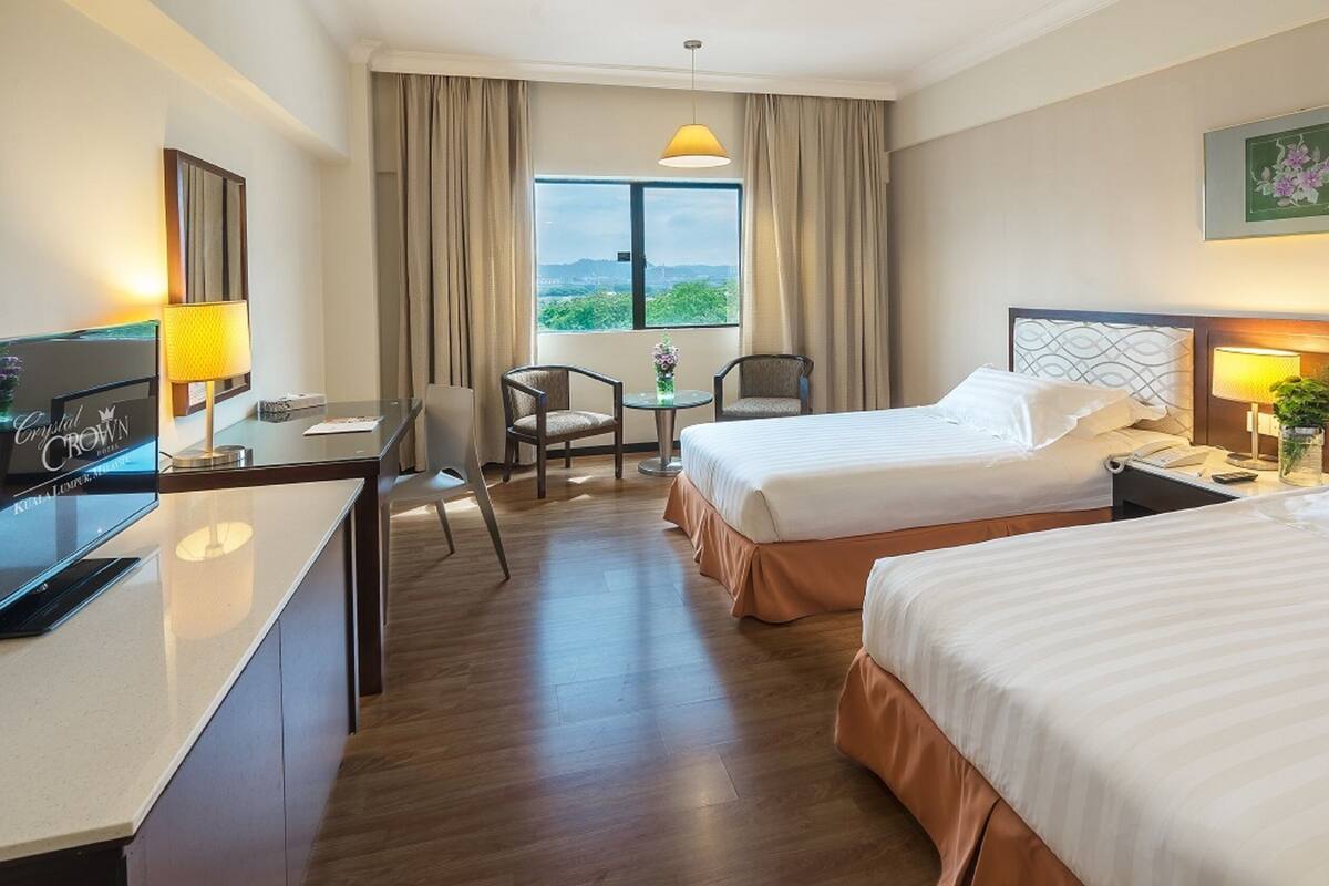 Une chambre d’hôtel avec deux lits, un bureau, une chaise, une petite table avec un vase et une fenêtre avec des rideaux.