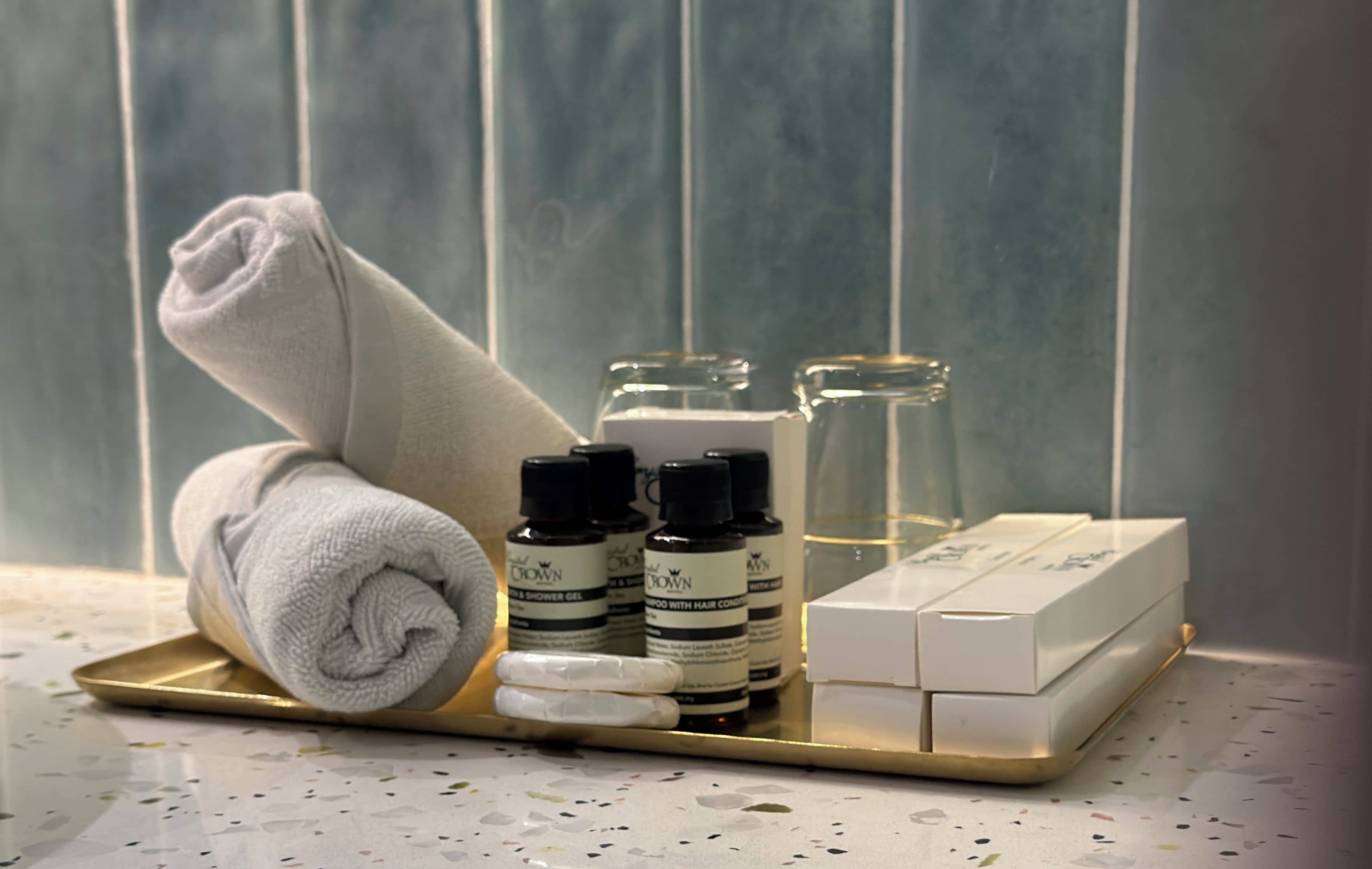 Un tocador de baño con artículos de aseo, incluyendo una toalla, botellas de productos para el cabello y un vaso de agua.