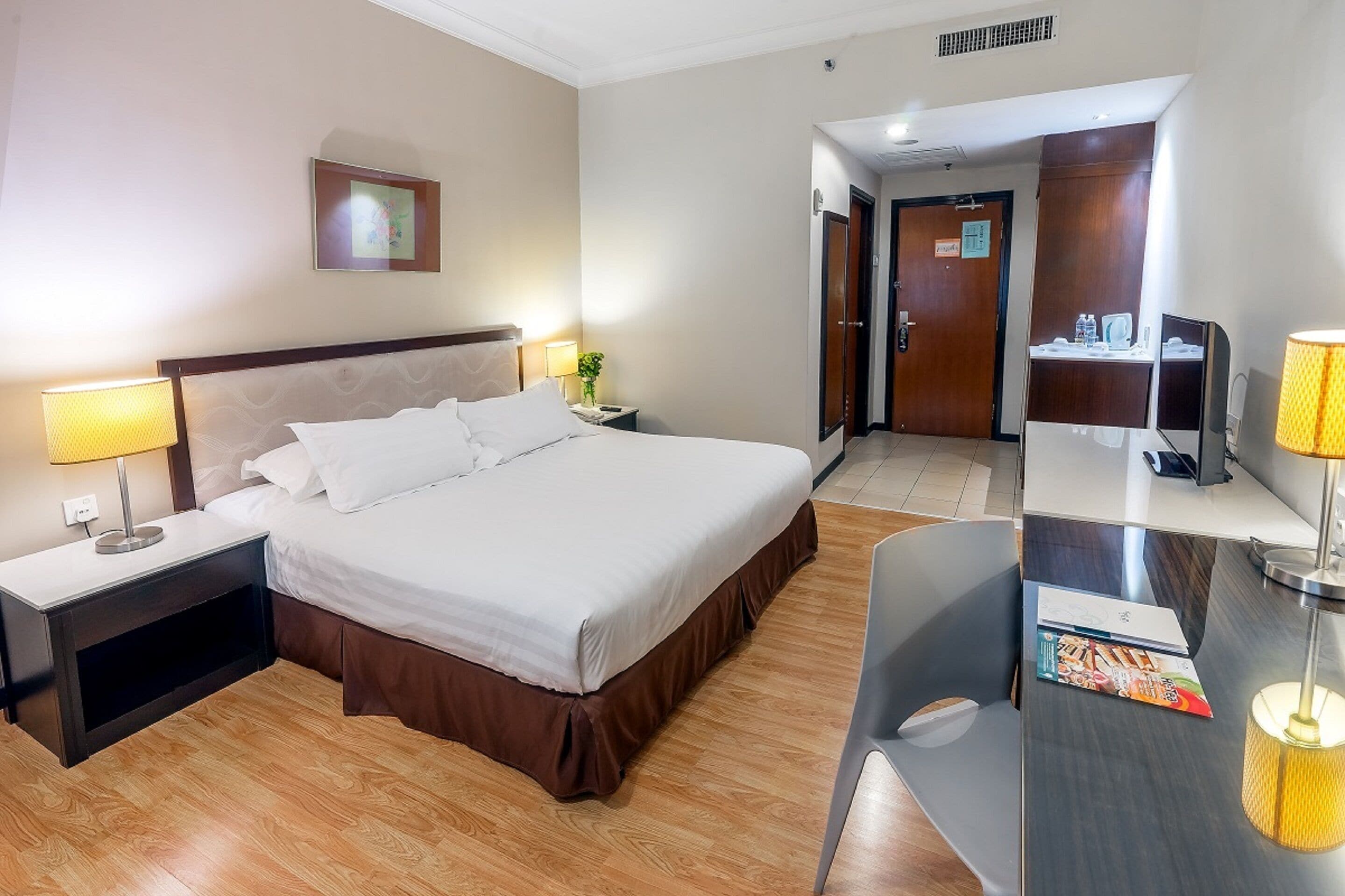 A hotel room with a large bed, bedside tables with lamps, a desk with a chair, and a mirror.