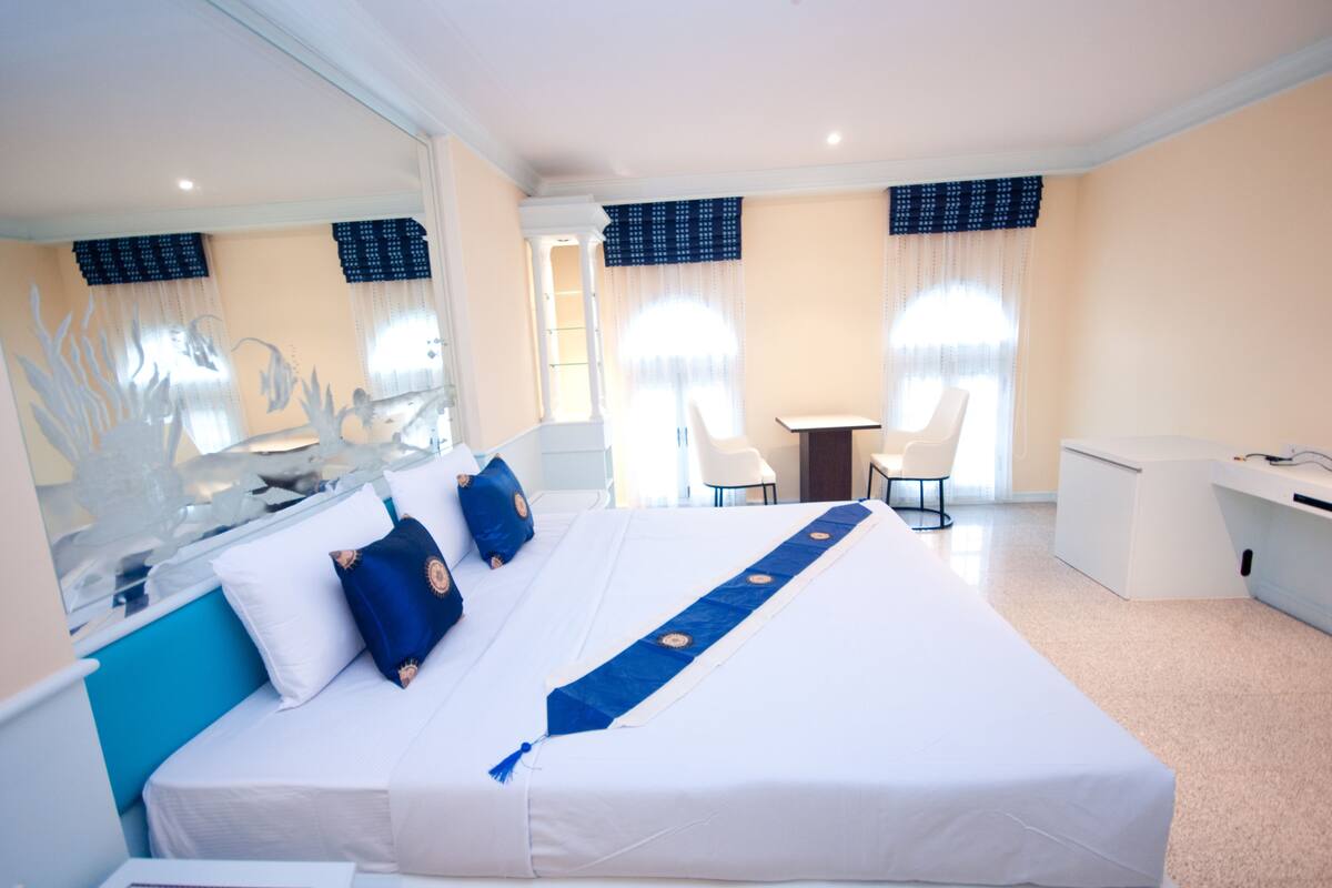 A hotel room with a large bed, a desk, a chair, and a small table.