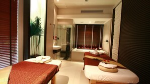 A spa room with two massage tables, a large mirror, and a window with blinds. - Siam Paradise Entertainment Complex (Bangkok)