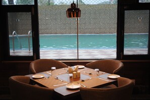 A dining table with chairs, a pool view, and a hanging light fixture. - Welcome Hotel at Srinagar (Srinagar)