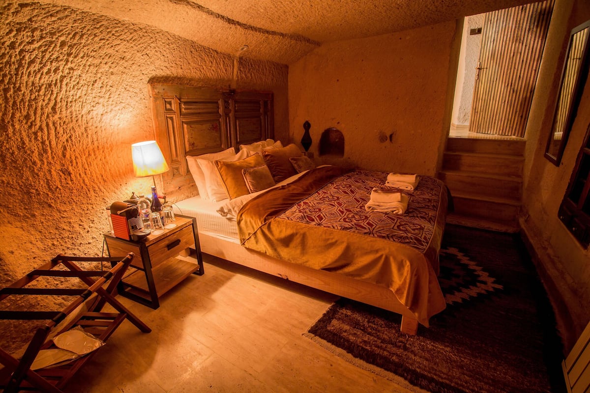 Une chambre confortable avec un lit en bois, une table de chevet, une lampe et un mur en pierre rustique.