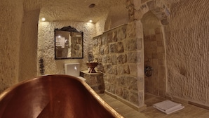 A stone-walled bathroom with a bathtub, a mirror, and a sink.