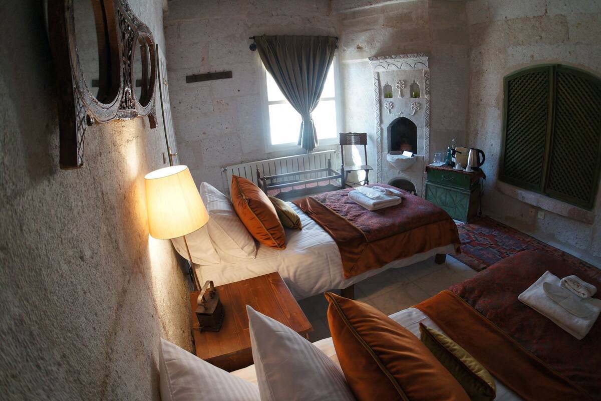 Une chambre rustique avec deux lits, une fenêtre avec un rideau, un radiateur, une table de chevet en bois et une commode verte.