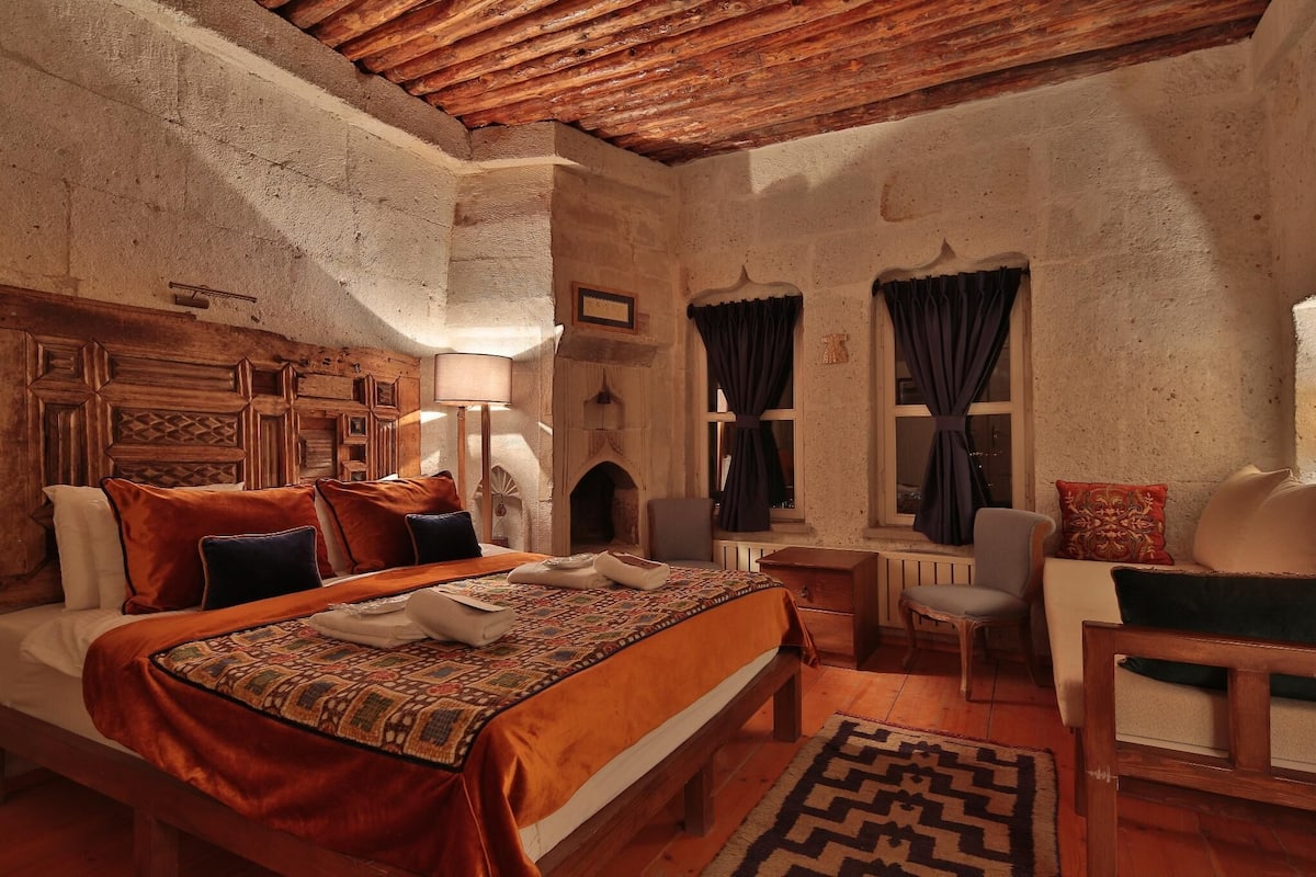 Une chambre à coucher au style rustique, avec une tête de lit en bois, un grand lit recouvert d’une literie à motifs, un banc en bois et une chaise.