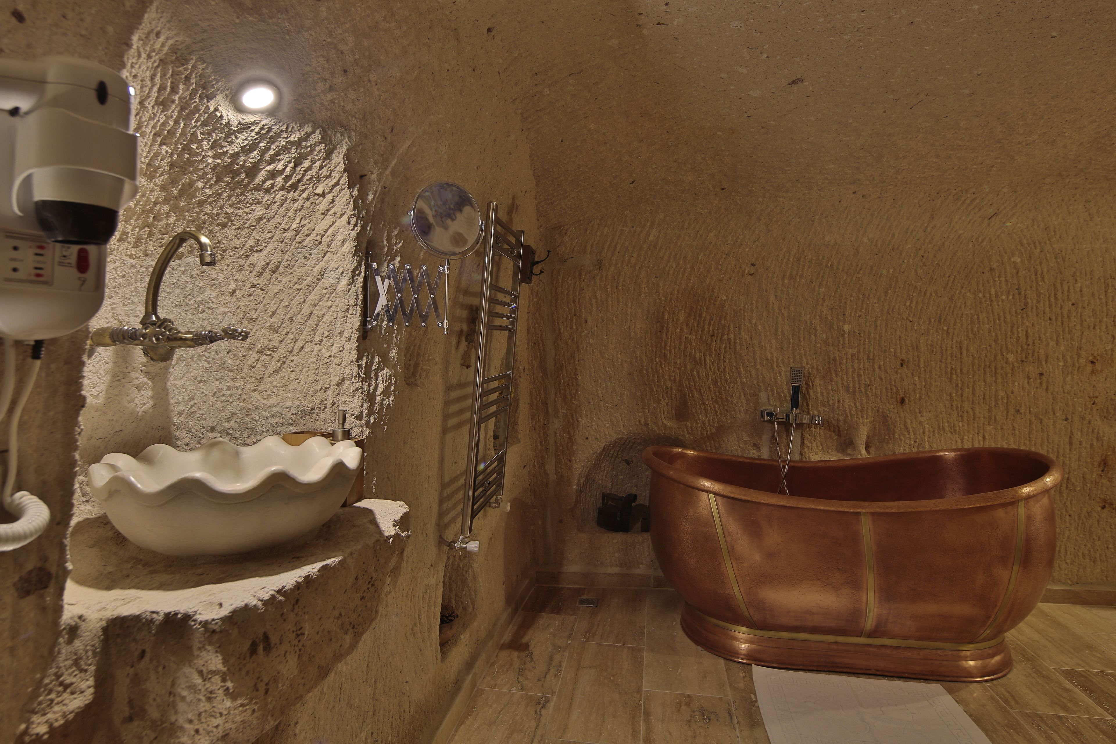 Un baño con lavamanos blanco, bañera de cobre y espejo.