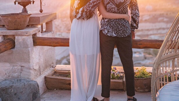 A couple standing on a balcony overlooking a sunset with hot air balloons in the sky.