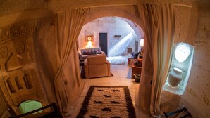 A cozy, stone-walled room with a rustic wooden bench, a plush sofa, and a patterned rug.