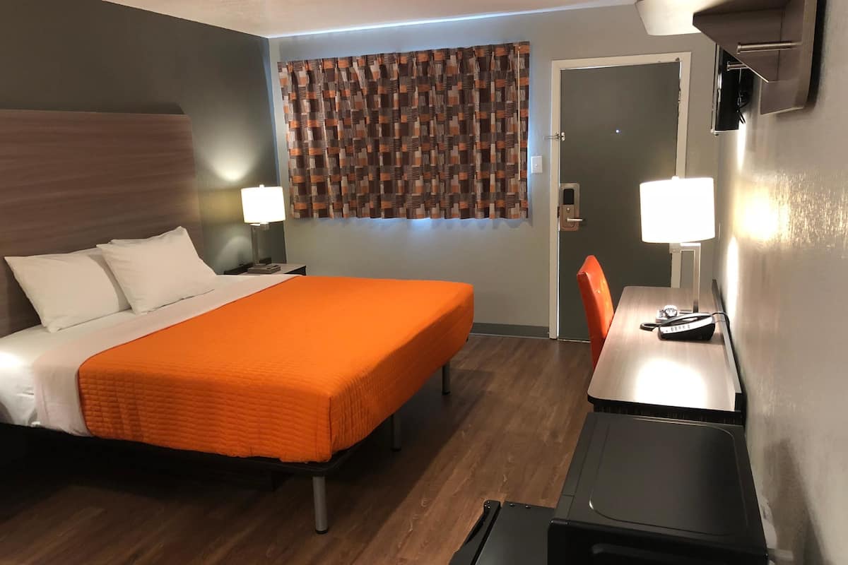 Quarto de hotel com cama, escrivaninha, cadeira e janela com cortinas.