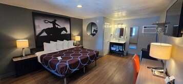 Habitación de hotel con una cama grande, lámparas de noche, un escritorio con teléfono, un espejo y un aire acondicionado de pared.