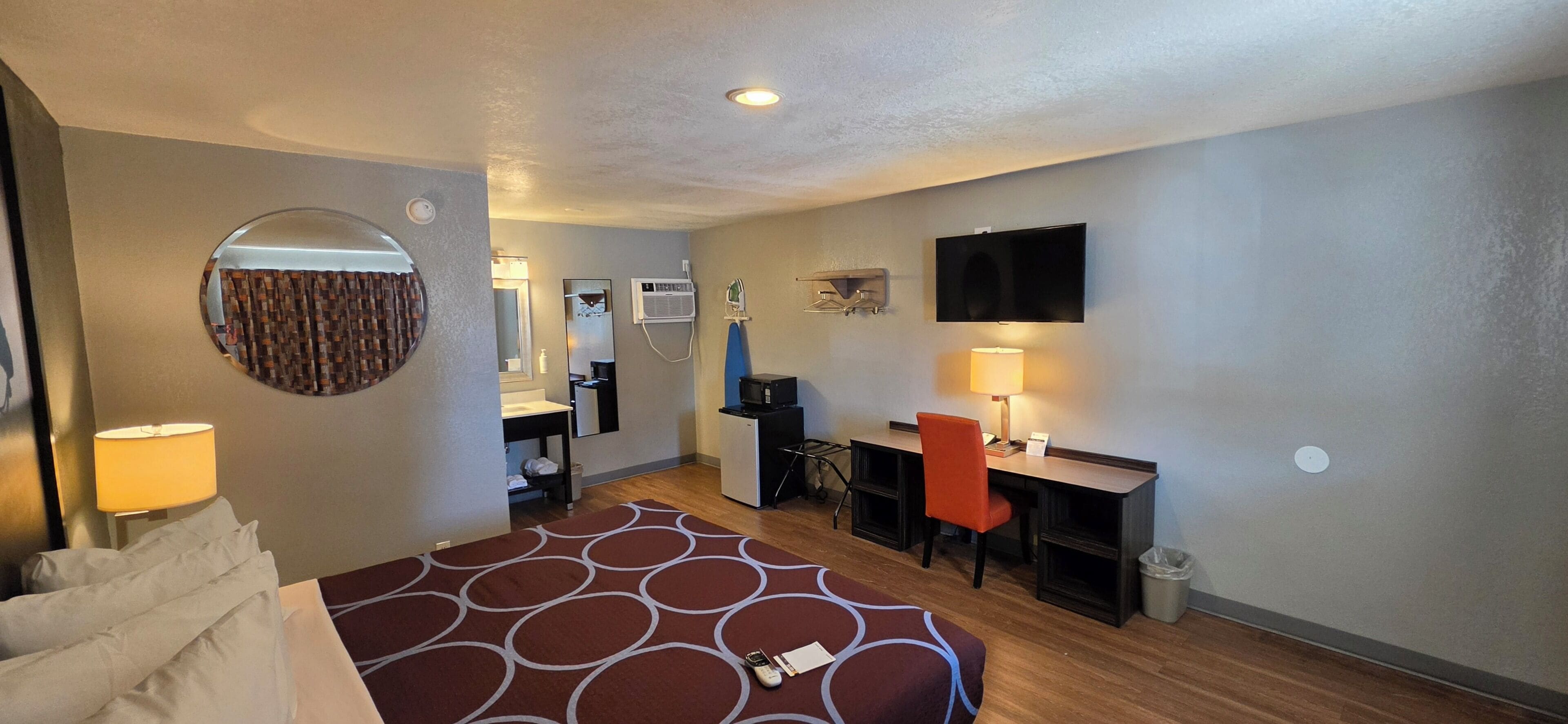 A hotel room with a bed, desk, chair, TV, and a mirror.