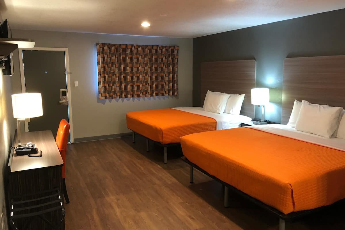 Quarto de hotel com duas camas de solteiro, uma mesa com cadeira e uma pequena mesa com abajur.