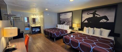 A hotel room with two beds, a desk with a lamp, a mirror, and a mounted TV.