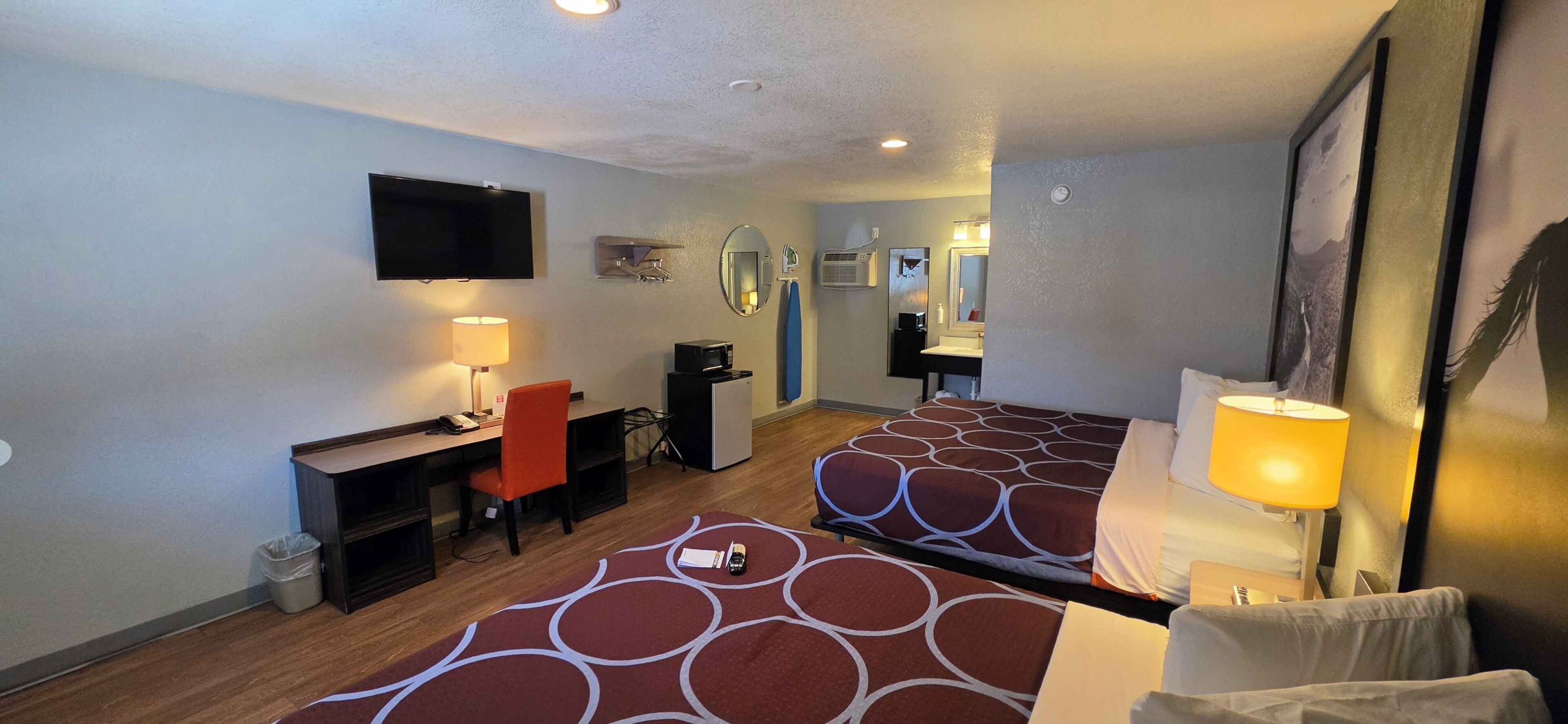A hotel room with two beds, a desk, a chair, a TV, a mirror, and a lamp.
