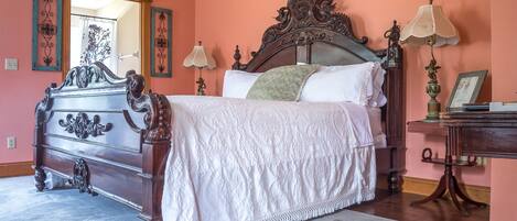 A bedroom with a large bed, ornate dresser, and a mirror.
