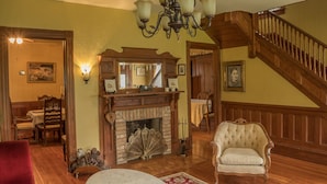 Un salón tradicional con chimenea, suelo de madera, una escalera y muebles clásicos.