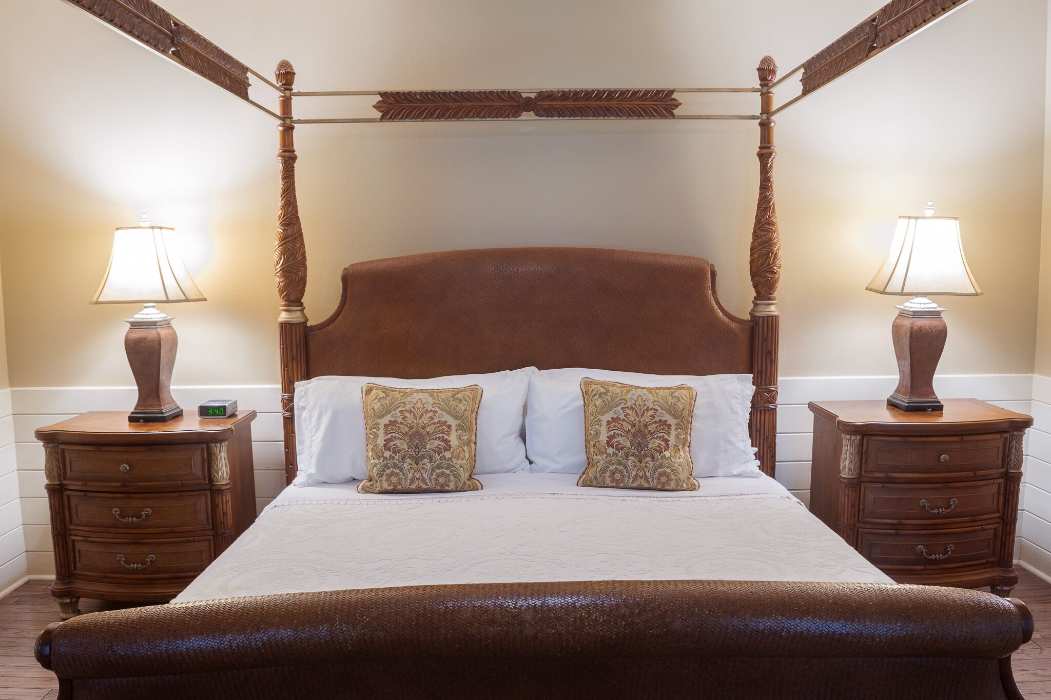 A four-poster bed with white linens and decorative pillows, flanked by wooden nightstands with lamps.