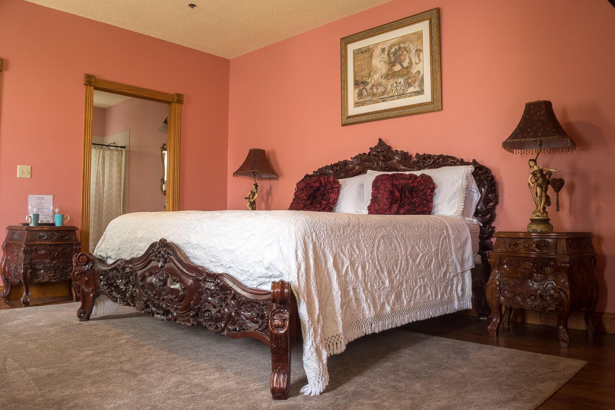 A bedroom with a large bed, two nightstands, a mirror, and a painting on the wall.