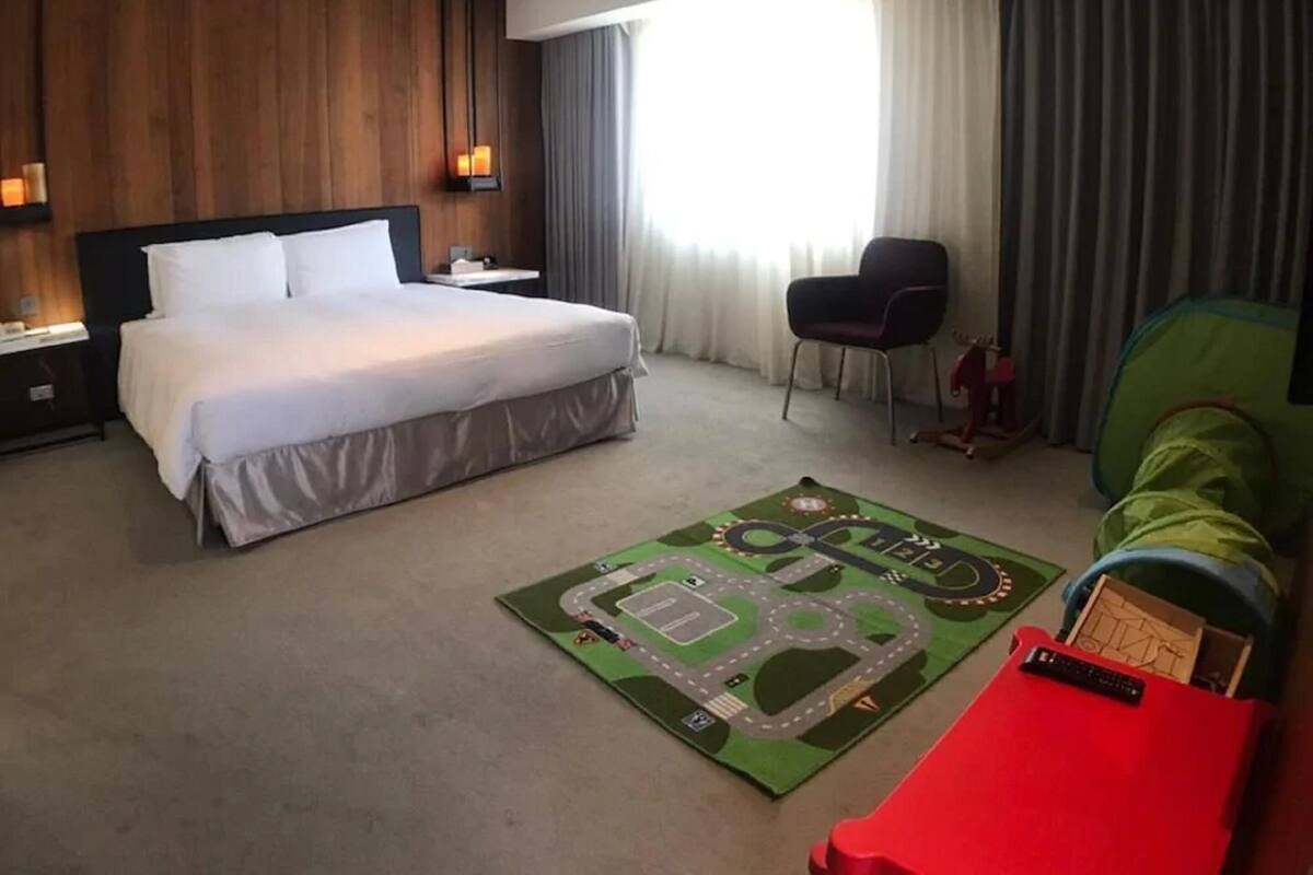 Habitación de hotel con una cama grande, un escritorio, una silla, un sofá verde y una carpa de juegos para niños.