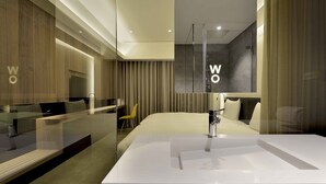A modern hotel bathroom with a large white sink, a glass shower enclosure, and a bed with a headboard. - Wo (Kaohsiung)