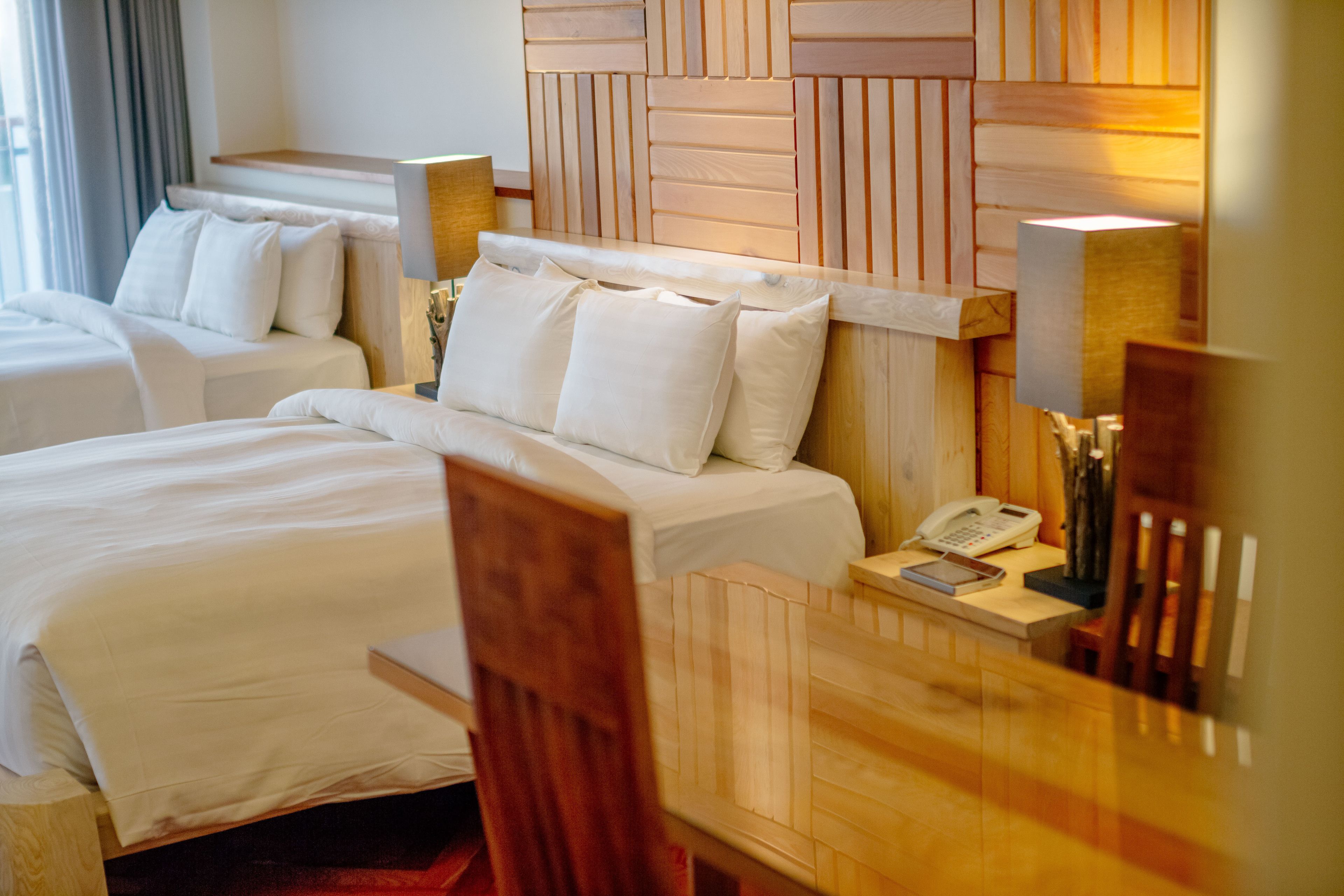 A hotel room with two beds, a wooden headboard, a desk with a phone, and a lamp.