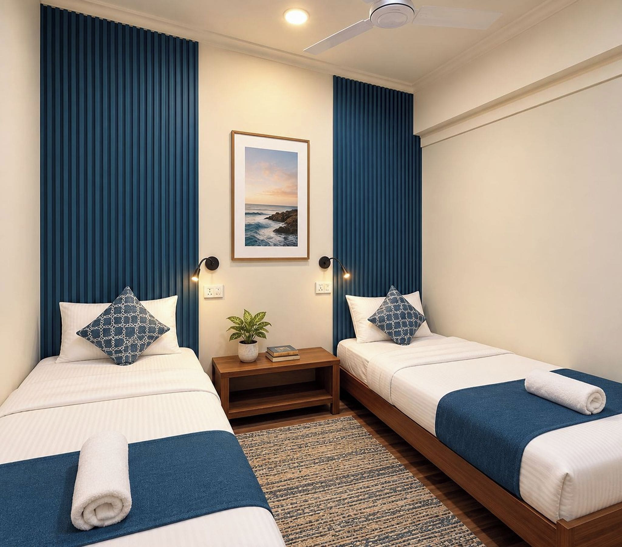 Habitación de hotel con dos camas, ventilador de techo, un cuadro en la pared y una pequeña mesa con una planta.