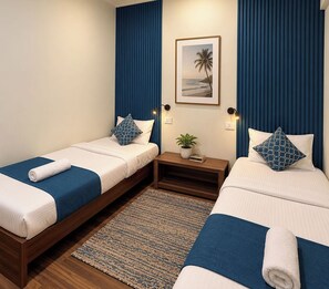 A hotel room with two single beds, a small bedside table with a plant, and a framed picture on the wall.