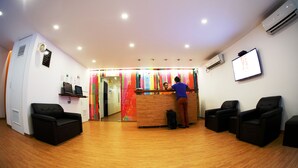 A reception area with a wooden floor, a reception desk, black leather chairs, and an air conditioning unit. - CityRest Fort - Hostel (Colombo)