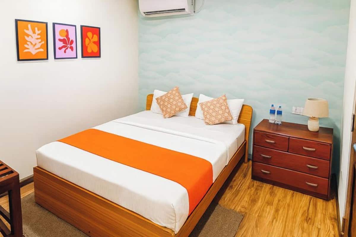 A bedroom with a wooden bed, orange bedding, a nightstand with a lamp, and a wall-mounted air conditioner.