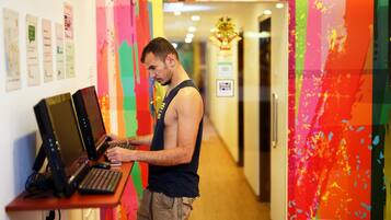 A man working at a desk with multiple laptops in a brightly colored hallway with posters on the wall.
