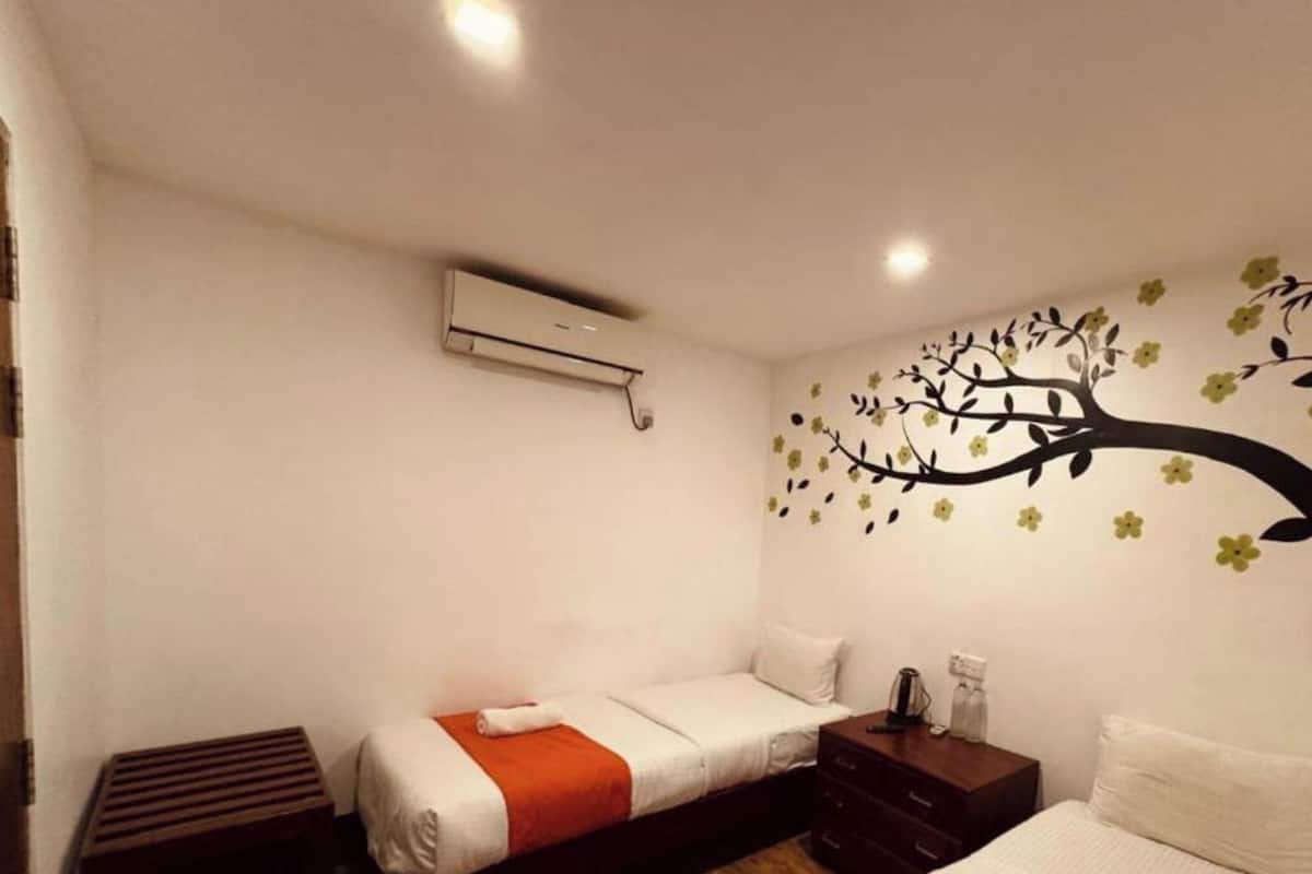 A hotel room with two beds, a wooden floor, a wall-mounted air conditioner, and a decorative tree mural.