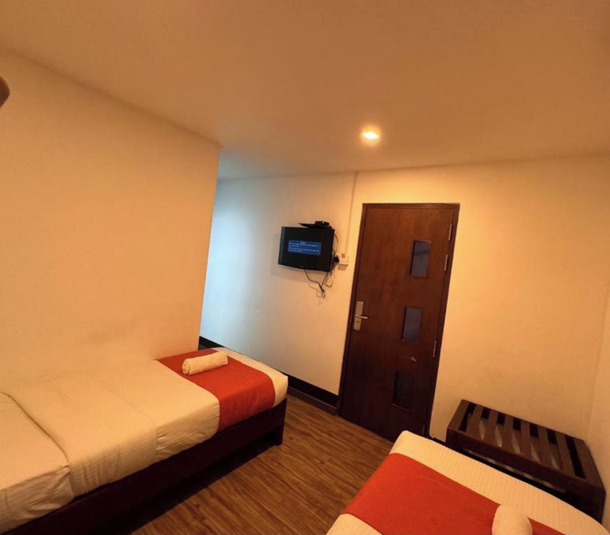 A hotel room with two beds, a television mounted on the wall, and a wooden door.