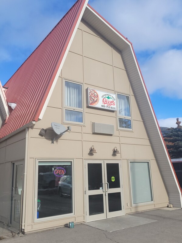 Un edificio con un letrero que dice 'Crowsnest Pass Pizza' y un letrero de neón que indica 'ABIERTO'.