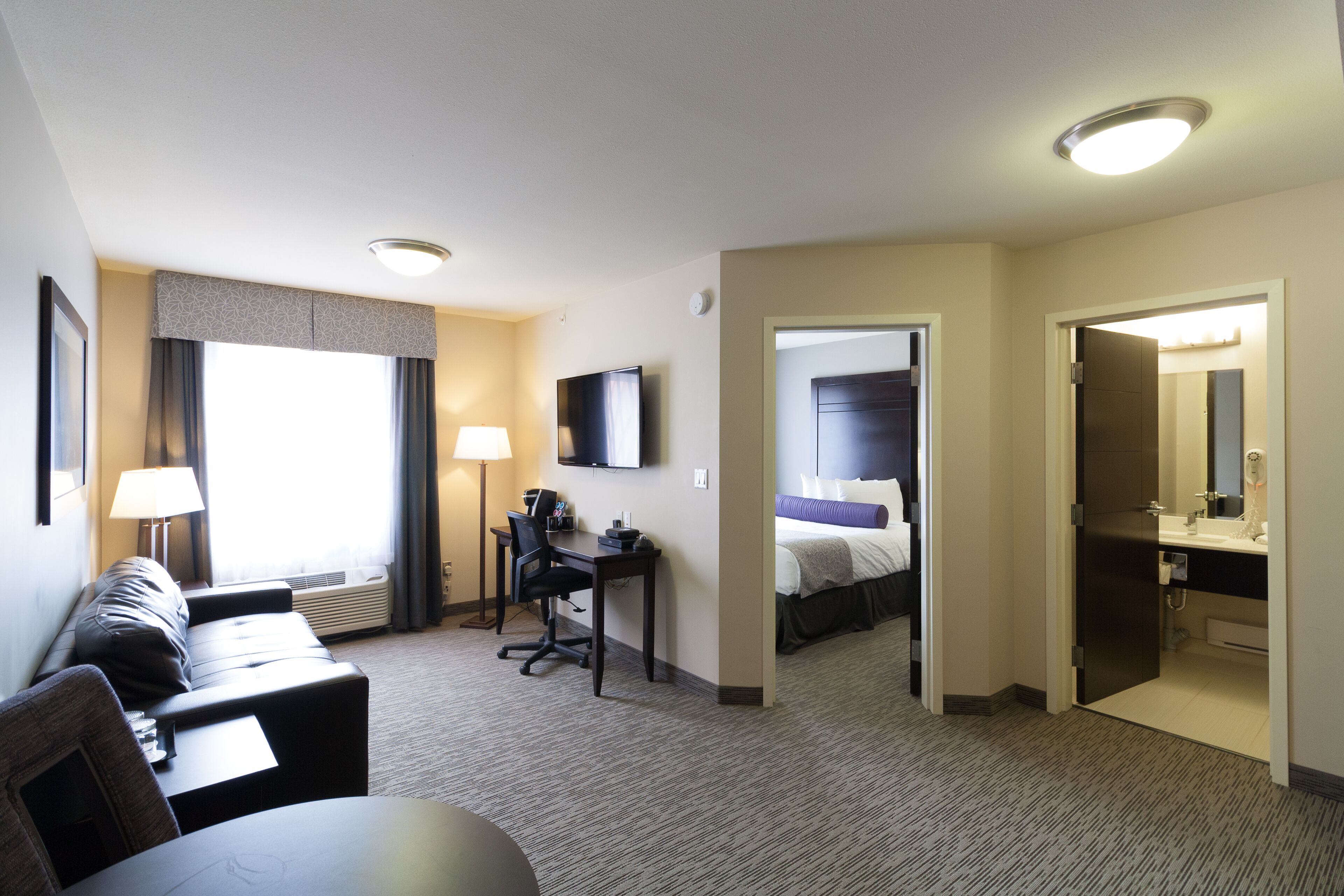 A hotel room with a sofa, desk, flat-screen TV, and a bed.