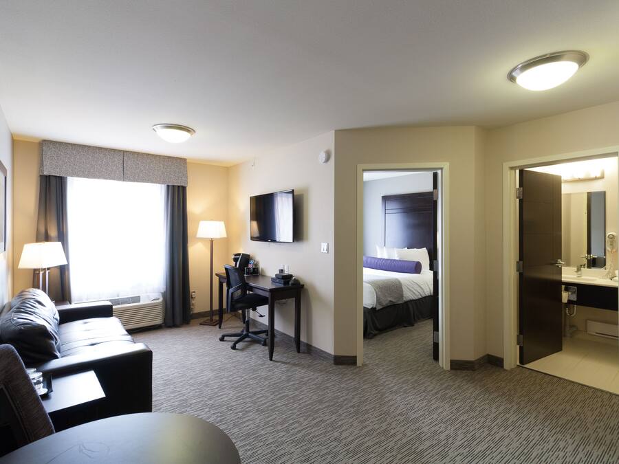 A hotel room with a sofa, desk, flat-screen TV, and a bed.