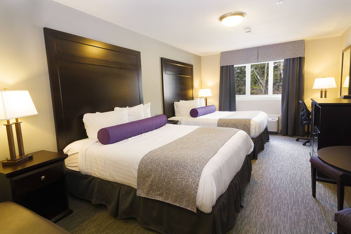 A hotel room with two beds, a desk, and a chair.