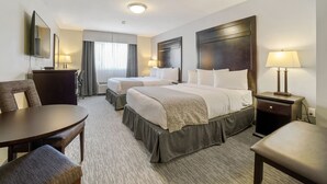 Habitación de hotel con dos camas, un escritorio, una silla, una lámpara y un espejo.